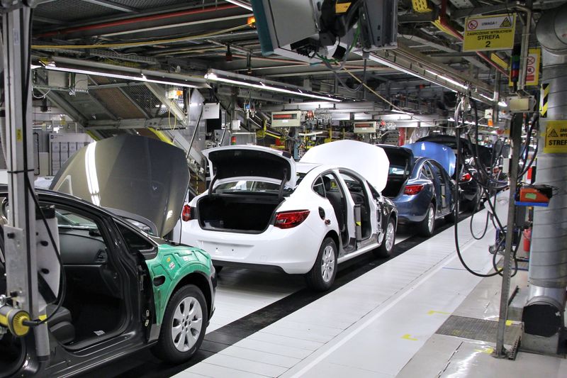 Cars on an assembly line at a General Motors manufacturing plant, with vehicle bodies in various stages of production under industrial lighting