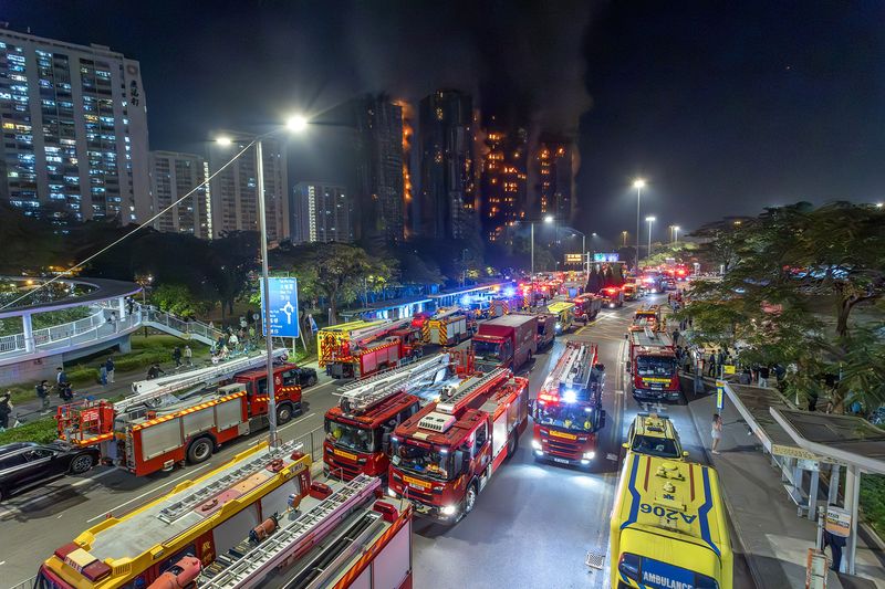 Fire engines and ambulances of the Hong Kong Fire Services Department line the road outside Wang Fuk Court as the residential tower burns at night in November 2025
