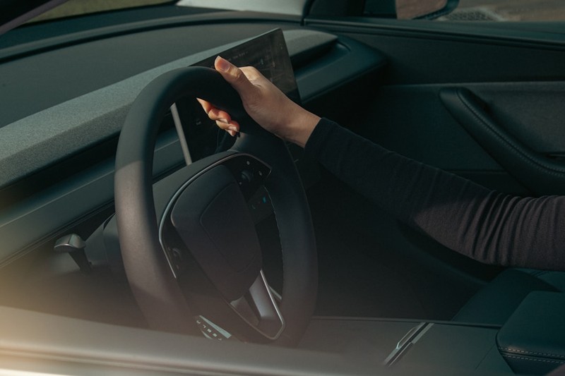 A driver's hand grips the steering wheel of a Tesla Model Y, highlighting the need for human oversight of autonomous driving systems