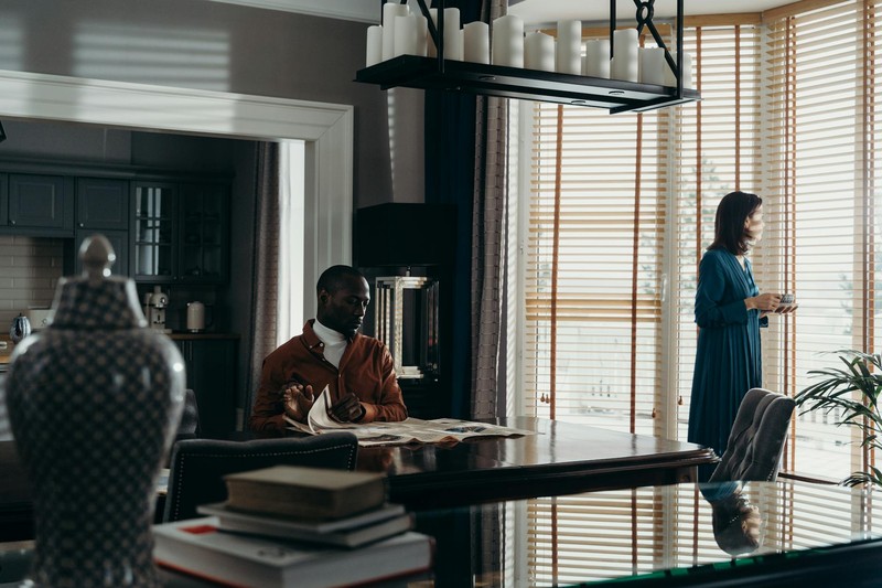 A man reads a newspaper while a woman gazes out the window in a stylish dining room.