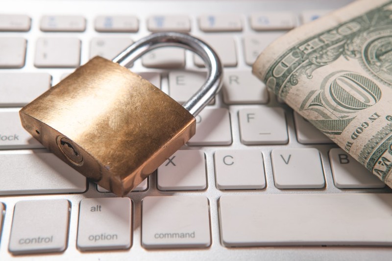 A brass padlock and a folded US dollar bill resting on a white computer keyboard