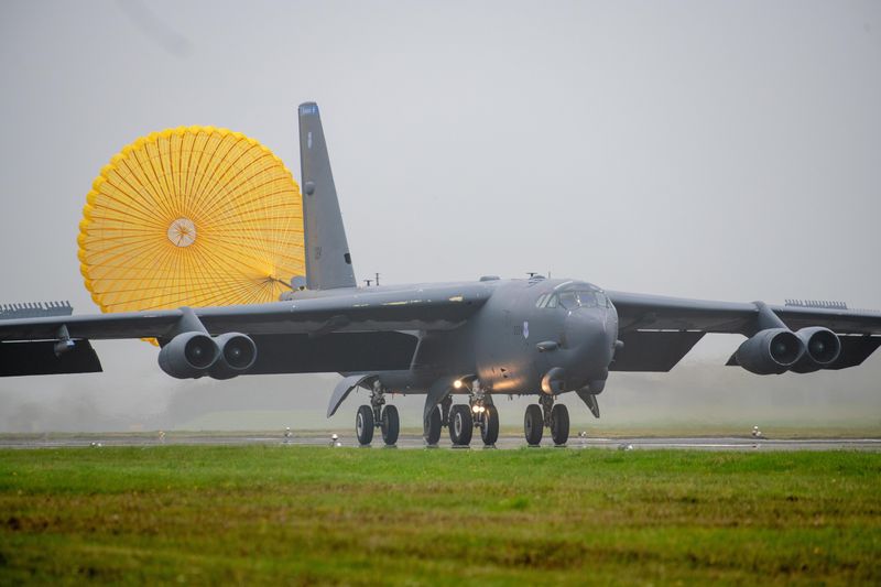 A B-52H Stratofortress bomber landing at RAF Fairford, England, with its yellow braking parachute deployed on a misty airfield