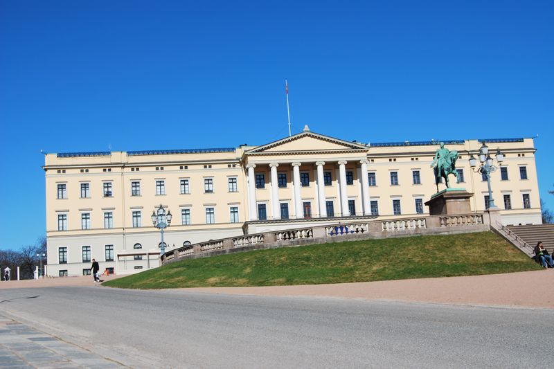 The Royal Palace in Oslo, Norway, a neoclassical building on a green hill with an equestrian statue, under a clear blue sky
