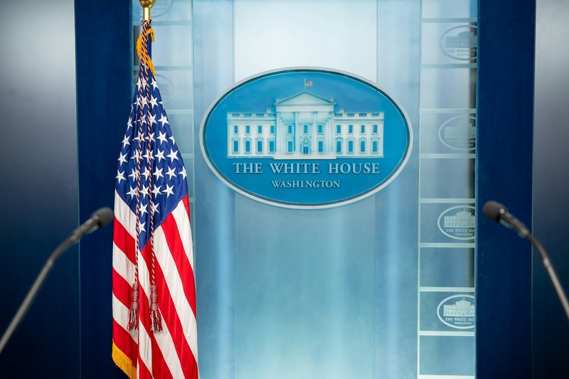 Empty White House press briefing podium with the presidential seal, American flag, and microphones