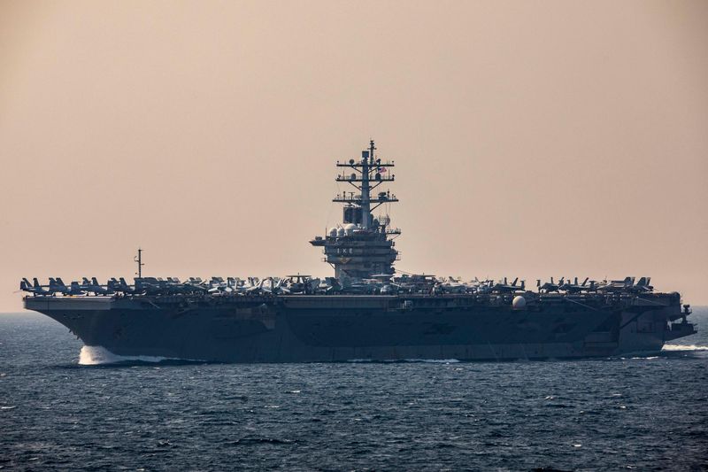 The aircraft carrier USS Dwight D. Eisenhower (CVN-69) transits the Strait of Hormuz, seen in profile against a hazy sky with aircraft visible on its flight deck