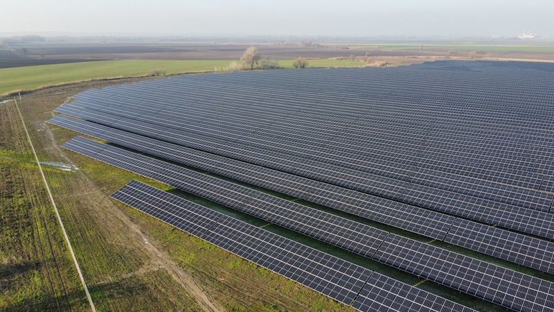 Aerial view of a vast solar farm with rows of photovoltaic panels stretching across open farmland