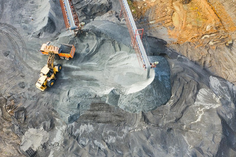 Aerial view of an open-pit mining operation with a front loader moving mineral ore alongside conveyor infrastructure