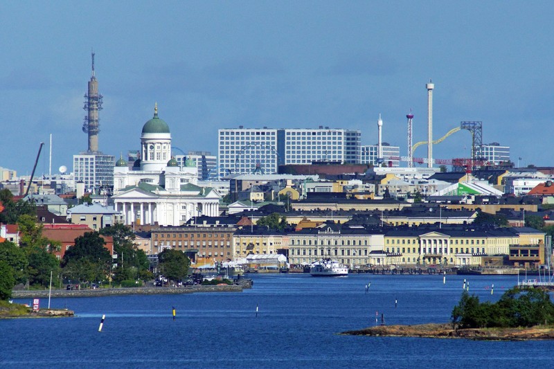 Helsinki skyline seen from across the water on a summer day, with the white Helsinki Cathedral and city buildings visible against a cloudy sky