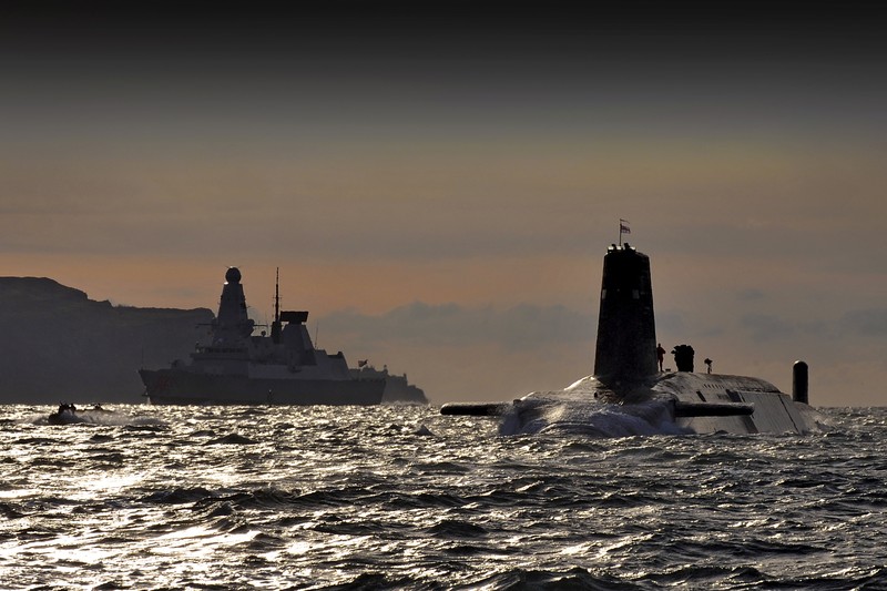 Nuclear submarine HMS Vanguard silhouetted against a dramatic sky as it returns to HM Naval Base Clyde at Faslane, Scotland, with HMS Dragon visible in the background