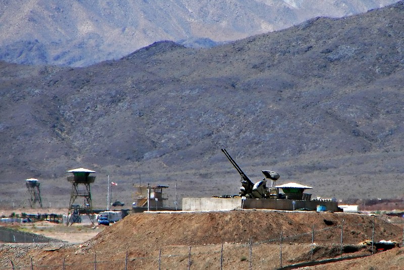 Anti-aircraft guns and guard towers defending Iran's Natanz nuclear facility, with arid mountains in the background