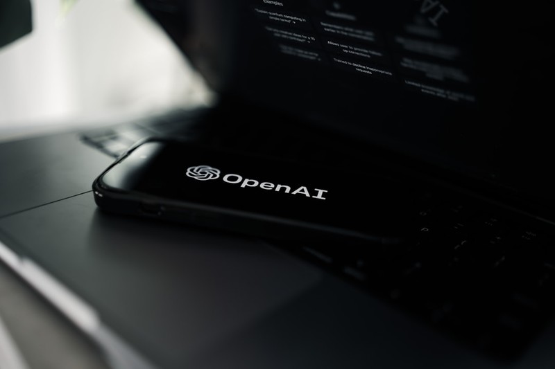 A smartphone displaying the OpenAI logo resting on a laptop keyboard