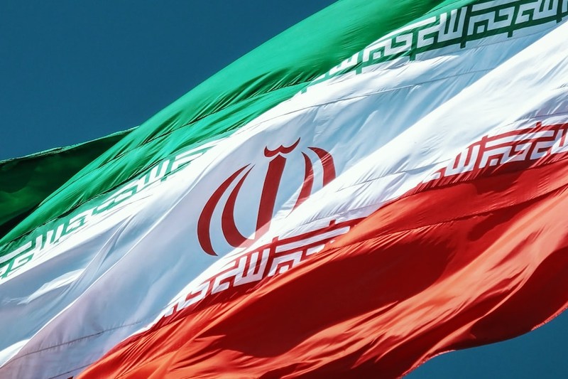 The flag of the Islamic Republic of Iran waving against a clear blue sky