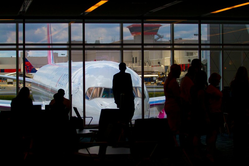 Silhouettes of travelers waiting at an airport terminal gate with a commercial airplane visible through the window