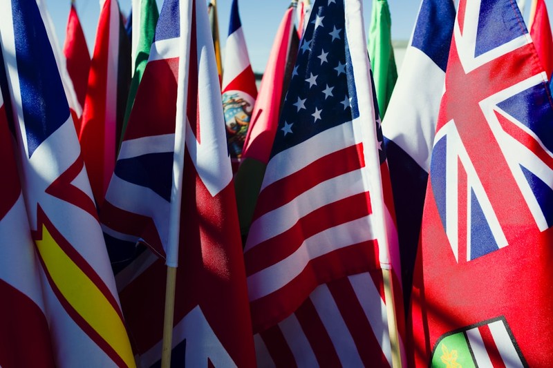 A collection of various national flags on wooden sticks displayed together outdoors, representing international diplomacy and multinational coalitions