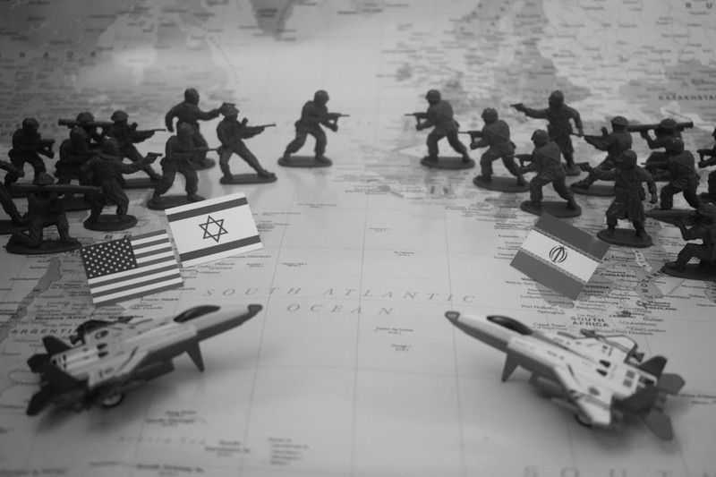 Toy soldiers and military jets arranged on a world map with American, Israeli, and Iranian flags depicting geopolitical conflict