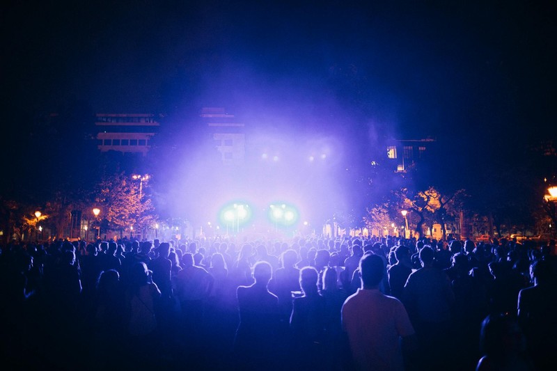 A massive crowd silhouetted against dramatic blue and purple stage lights at an outdoor night concert