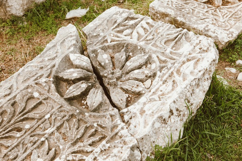Close-up of a cracked and broken ornamental stone carving lying on the ground, its intricate floral pattern split apart