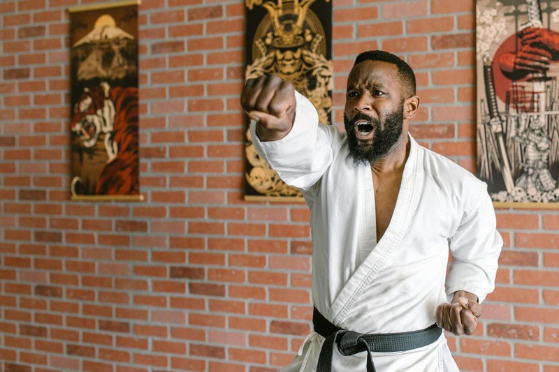 Martial artist in traditional white karate gi with black belt executing a powerful punch in a dojo with brick wall backdrop
