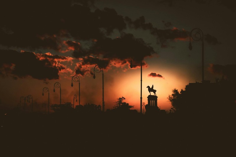 Silhouette of Havana at sunset with darkened street lamps and an equestrian statue against a dramatic sky
