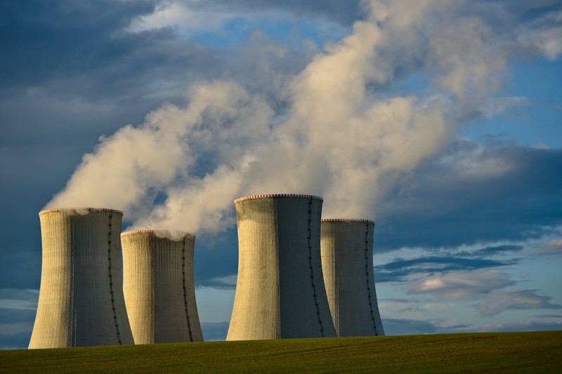 Nuclear power plant cooling towers emitting steam against a dramatic cloudy sky