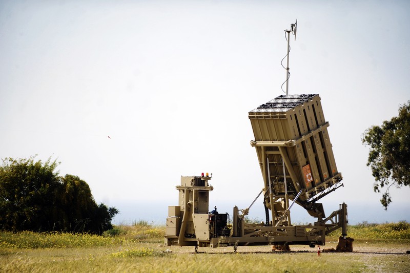 An Iron Dome air defense battery deployed in Israel, with its missile launcher angled upward and radar antenna on top, set against an overcast sky