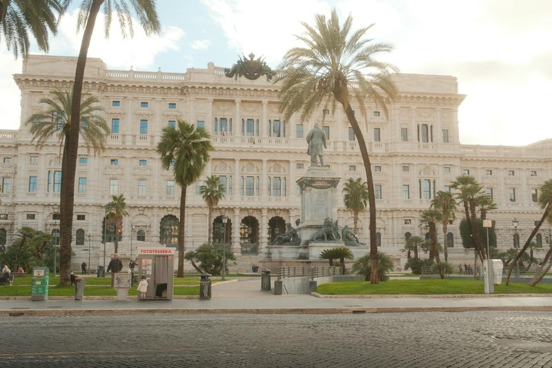 The neoclassical Palace of Justice in Rome, Italy, flanked by palm trees and fronted by a bronze monument