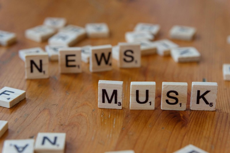 Close-up of wooden letter tiles on a table spelling 'News Musk', representing media coverage of Elon Musk