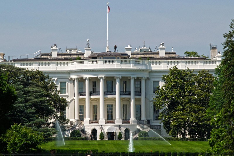 The White House south facade with surrounding gardens, fountains, and American flag flying overhead in Washington, D.C.