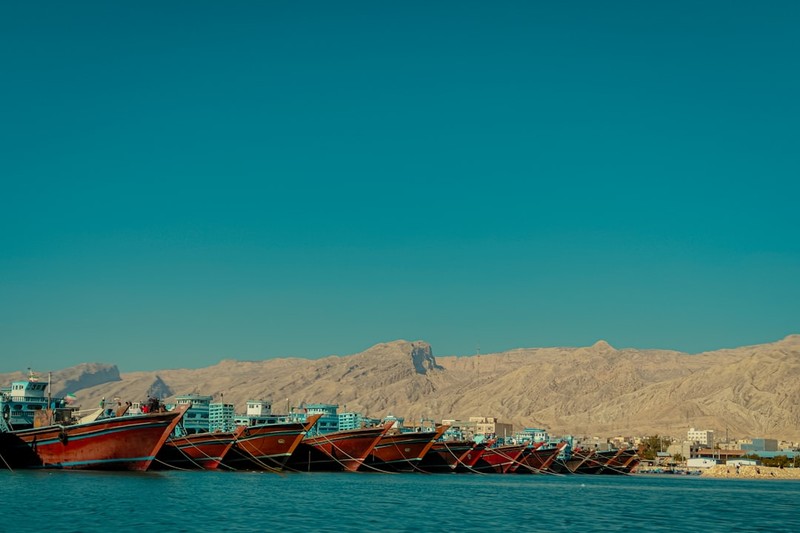 Cargo vessels moored at a port along the Persian Gulf with arid mountains rising in the background