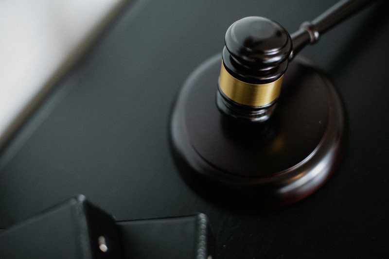 A wooden judge's gavel rests on a black desk surface