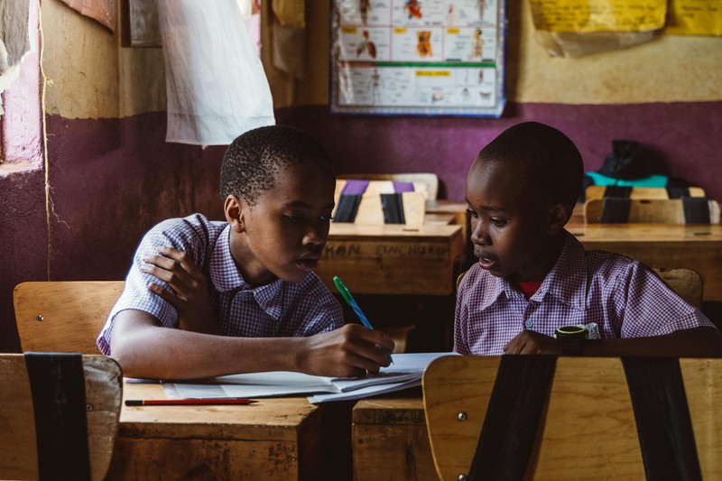 Two African schoolboys in matching uniforms work together on an assignment in a modest classroom
