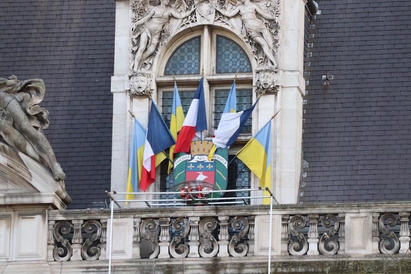 The ornate facade of Paris City Hall featuring French and Ukrainian flags displayed on the balcony, symbolizing municipal governance and international solidarity