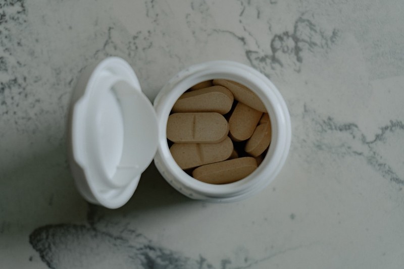An open pill bottle with beige tablets on a marbled surface