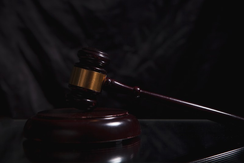 A wooden judge's gavel rests on a sounding block against a dark background.