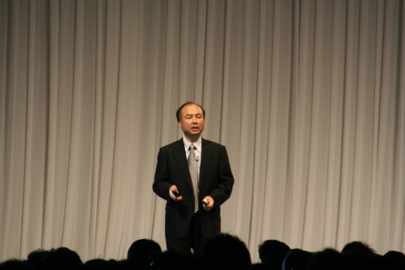 Masayoshi Son speaking at a podium with microphones at SoftBank Mobile Summit 2008