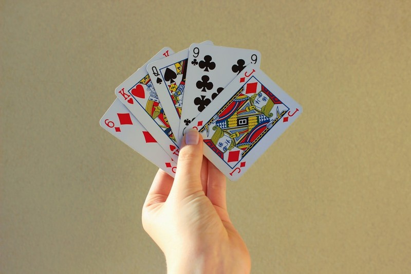 A hand holding a fan of five playing cards including King of Hearts, Queen of Spades, and Jack of Diamonds