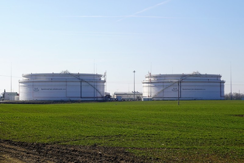 Large white oil storage tanks in a green field under clear blue sky