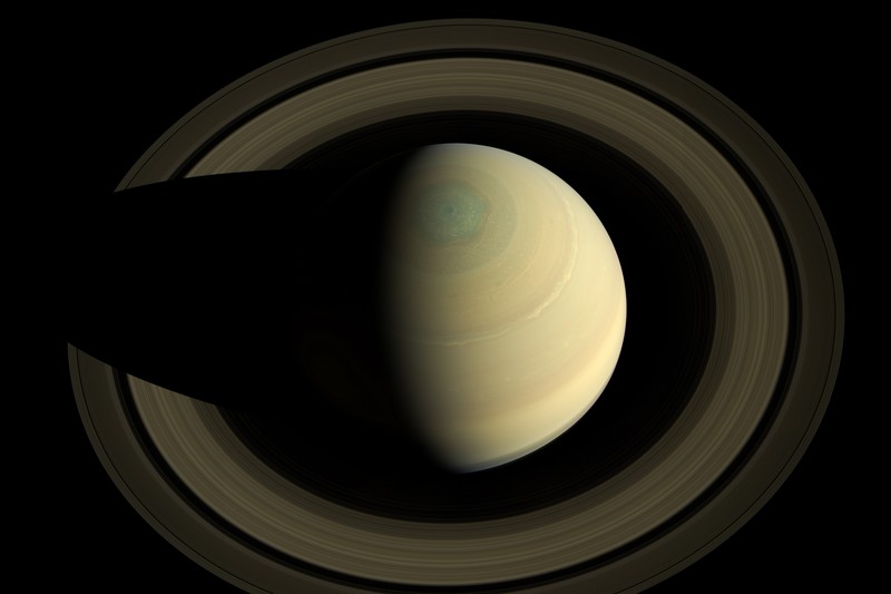 Saturn with its prominent ring system in natural color, showing the pale yellow planet with subtle atmospheric banding and multiple concentric rings against the black background of space