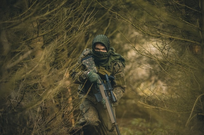 A soldier in tactical gear holding a rifle in a dense forest