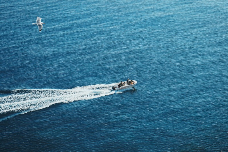 Aerial view of a small motorboat with passengers creating a white wake across open blue water