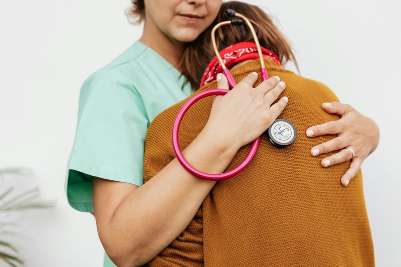 A healthcare professional in scrubs embraces a patient, providing comfort and support