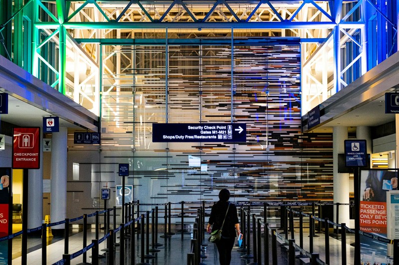 A traveler walks toward an airport security checkpoint with blue directional signage visible