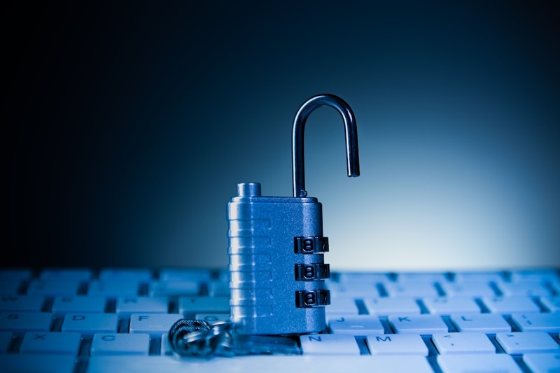 An open combination padlock sitting on a backlit computer keyboard, symbolizing compromised digital security