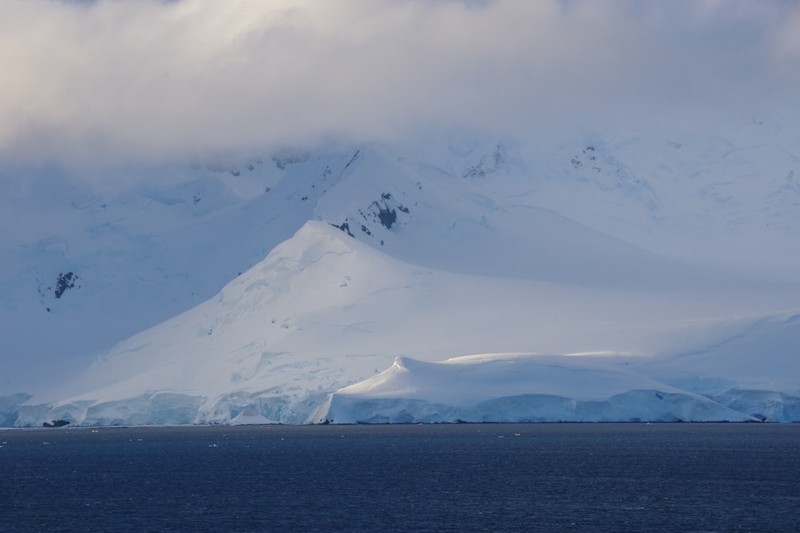 Snow-covered Antarctic mountains rise above the dark Southern Ocean under overcast skies