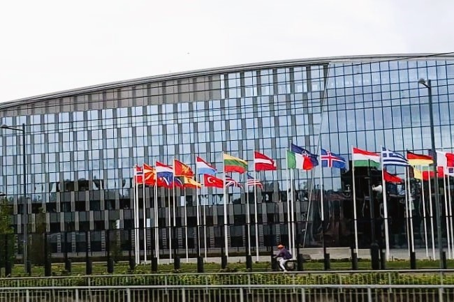 NATO headquarters building in Brussels with flags of member nations displayed along the front plaza