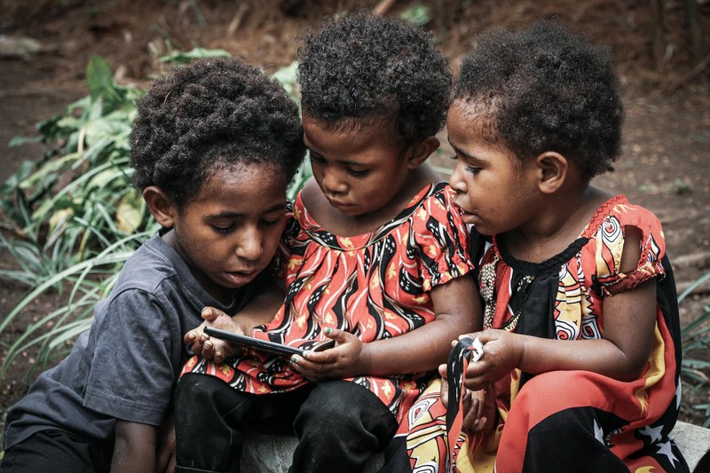 Three young children gathered together outdoors, sharing and looking at a smartphone