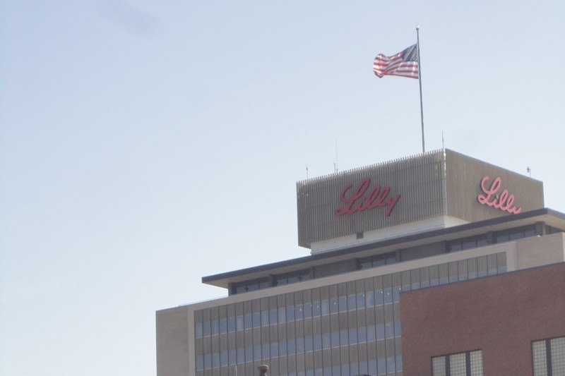 Eli Lilly corporate headquarters building with red Lilly signage and American flag against a clear blue sky