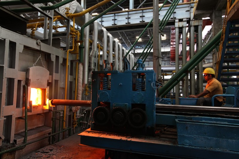 Worker monitoring a furnace with glowing hot metal in an industrial smelting facility