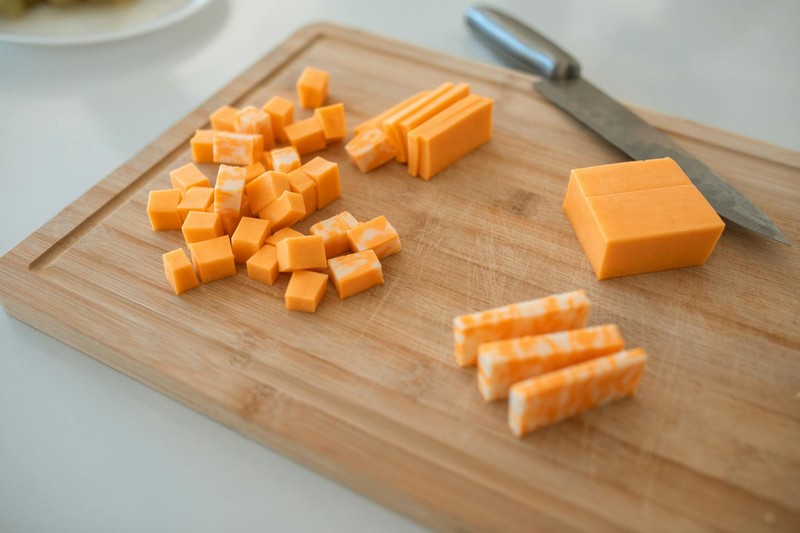 Cheddar cheese slices and cubes arranged on a wooden cutting board with a knife