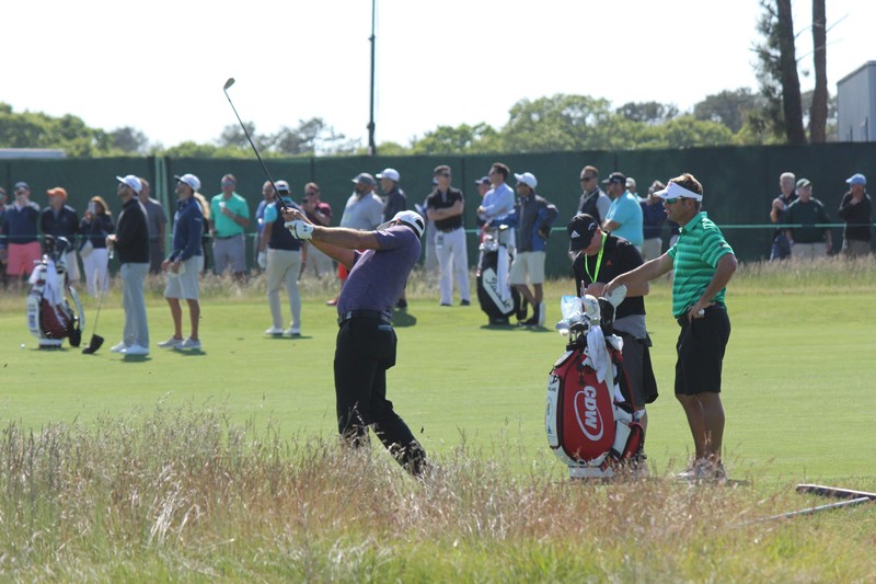 Gary Woodland swings a golf club during a tournament round with spectators and caddies watching